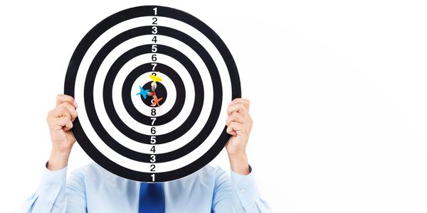 Person in blue shirt holds dartboard with three darts hitting near center.
