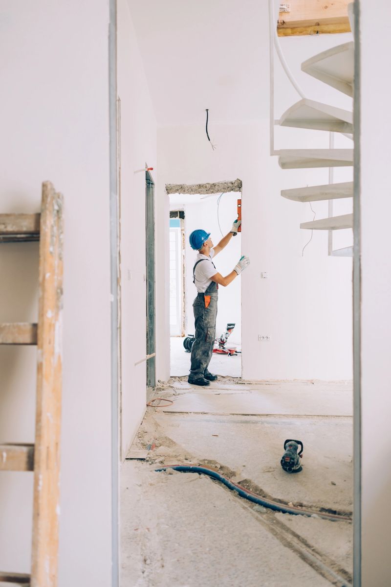 A construction worker wearing a blue helmet using a leveling tool for walls inside an apartment.