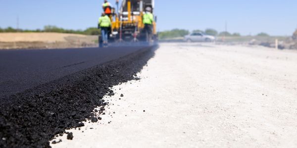 Workers paving a new asphalt road on a sunny day.