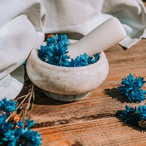 Hand dipping blue flowers into a stone bowl on a wooden surface.