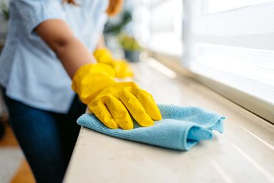 Person cleaning a countertop with a cloth and gloves.