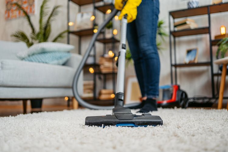 Person vacuuming a white carpet in a cozy living room.