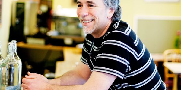 Smiling man in striped shirt leaning on a counter in a cozy cafe.