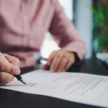 Person signing a document with a pen on a desk.