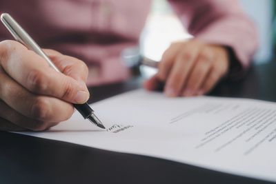 Person signing a document with a fountain pen on a desk.