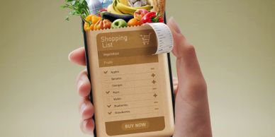 Hand holding a phone displaying a digital shopping list with fresh fruits and vegetables.