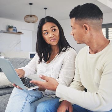 Couple discussing something on a laptop while sitting on a couch.