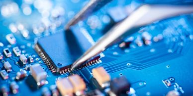 Close-up of a circuit board with tweezers near a chip.