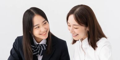 Two young women happily studying together with open books on a white table.