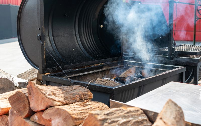 Pile of chopped wood with bbq smoker and smoke