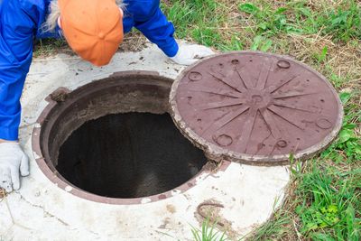 A worker in blue inspecting an open manhole outdoors.