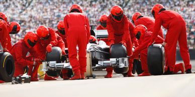 A Formula 1 pit crew in red suits changing tires during a race.