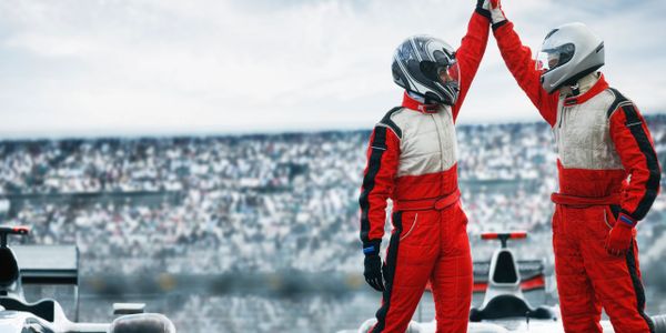 Two race car drivers celebrate their victory with a high five on the track.