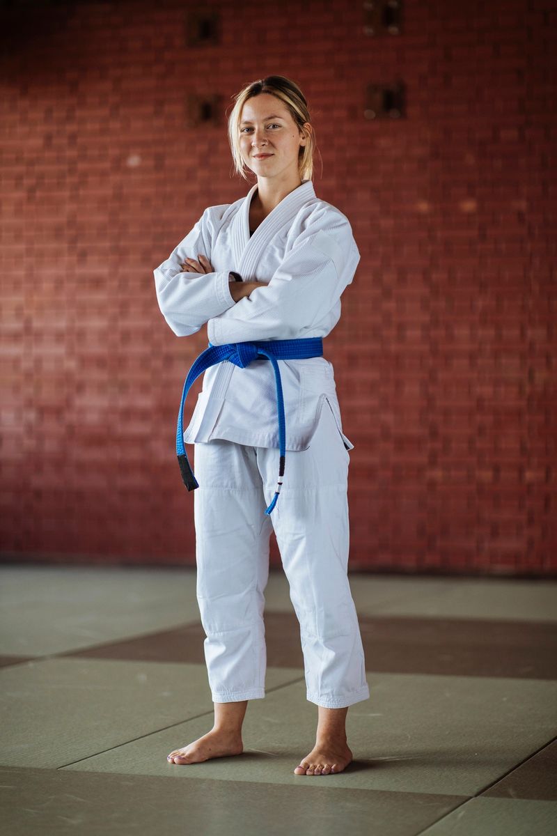 A young woman wearing a white kimono and a blue belt crossed her hands and looked at the camera