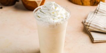A creamy vanilla milkshake topped with whipped cream in a clear plastic cup.