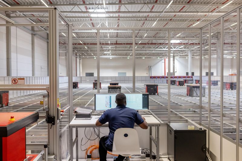 Rear view of a worker working in distribution warehouse with automated guided vehicles sorting the parcels in background. Man operating parcel sorting robot system in warehouse.