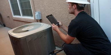 Technician inspecting an outdoor air conditioning unit with a tablet.