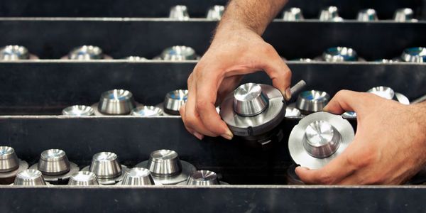 Hands handling metal components in an industrial setting.