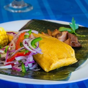 A traditional tamale served with corn, vegetables, and meat on a banana leaf.