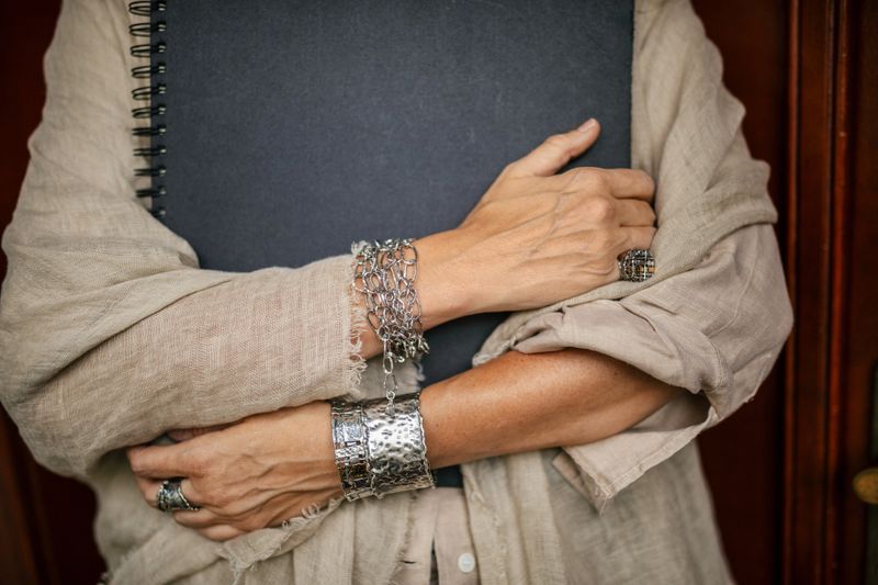 Mature adult woman holding book and wearing jewelry in her manufacture workshop. She is a designer and artist of unique jewelry made of precious metal. She is doing all process phases from design, manufacture and quality control