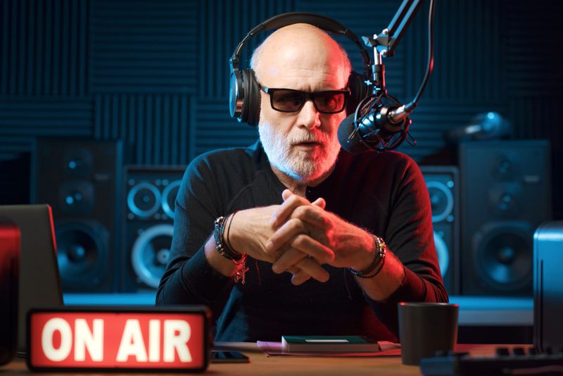 Professional expressive radio presenter working at the radio station, he is wearing headphones and talking into the microphone