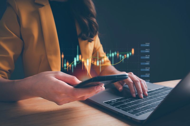 Businesswoman or trader using smartphone, showing a growing virtual hologram stock on computer laptop. Concept of planning and strategy, Stock market, Business growth, progress, trading or success.
