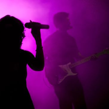 Silhouettes of a singer and guitarist in purple stage fog.