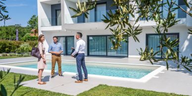 Three people talking near a backyard pool outside a modern house.