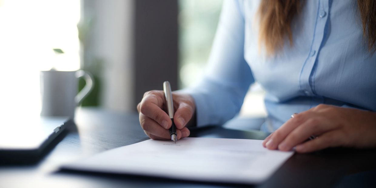 Person in blue shirt signing a document at a desk.