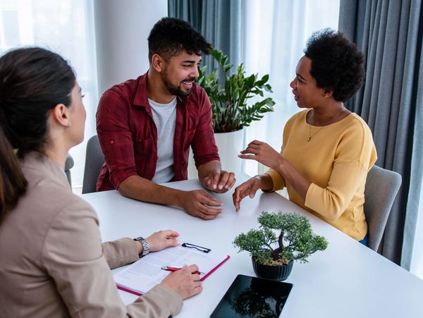 Three people engaged in a lively discussion at a white table indoors.