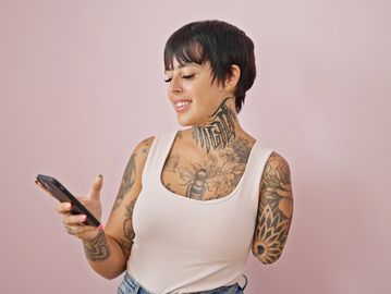 a woman smiling. has short dark hair, tattoos and a tank top. she is a left arm amputee at the elbow
