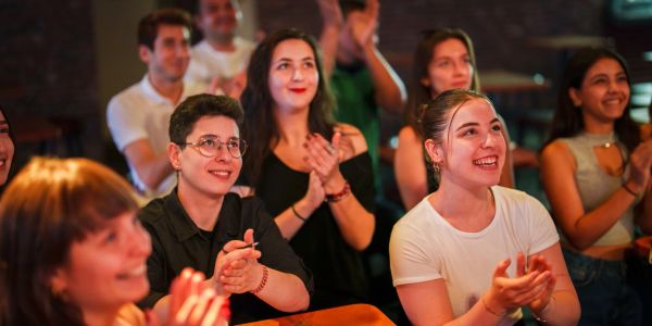 A group of people happily clapping and enjoying an event indoors.