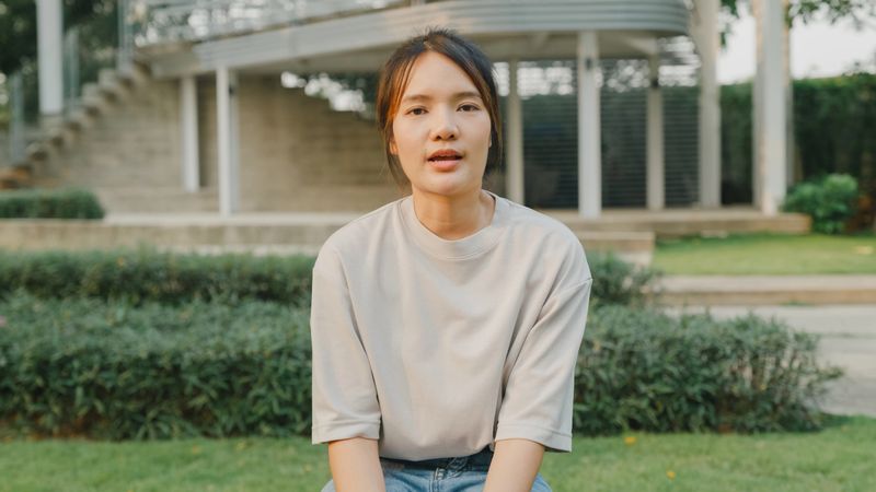 Young Asian woman looking at camera share experience of mental health in park. Mental health concept.