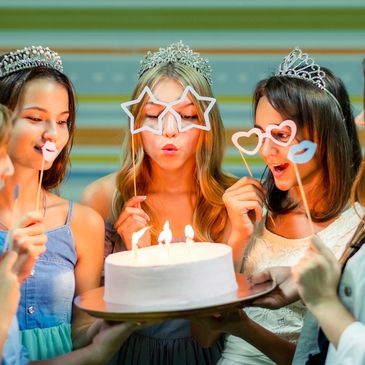 Girls with tiaras celebrating a birthday with a cake and fun glasses.