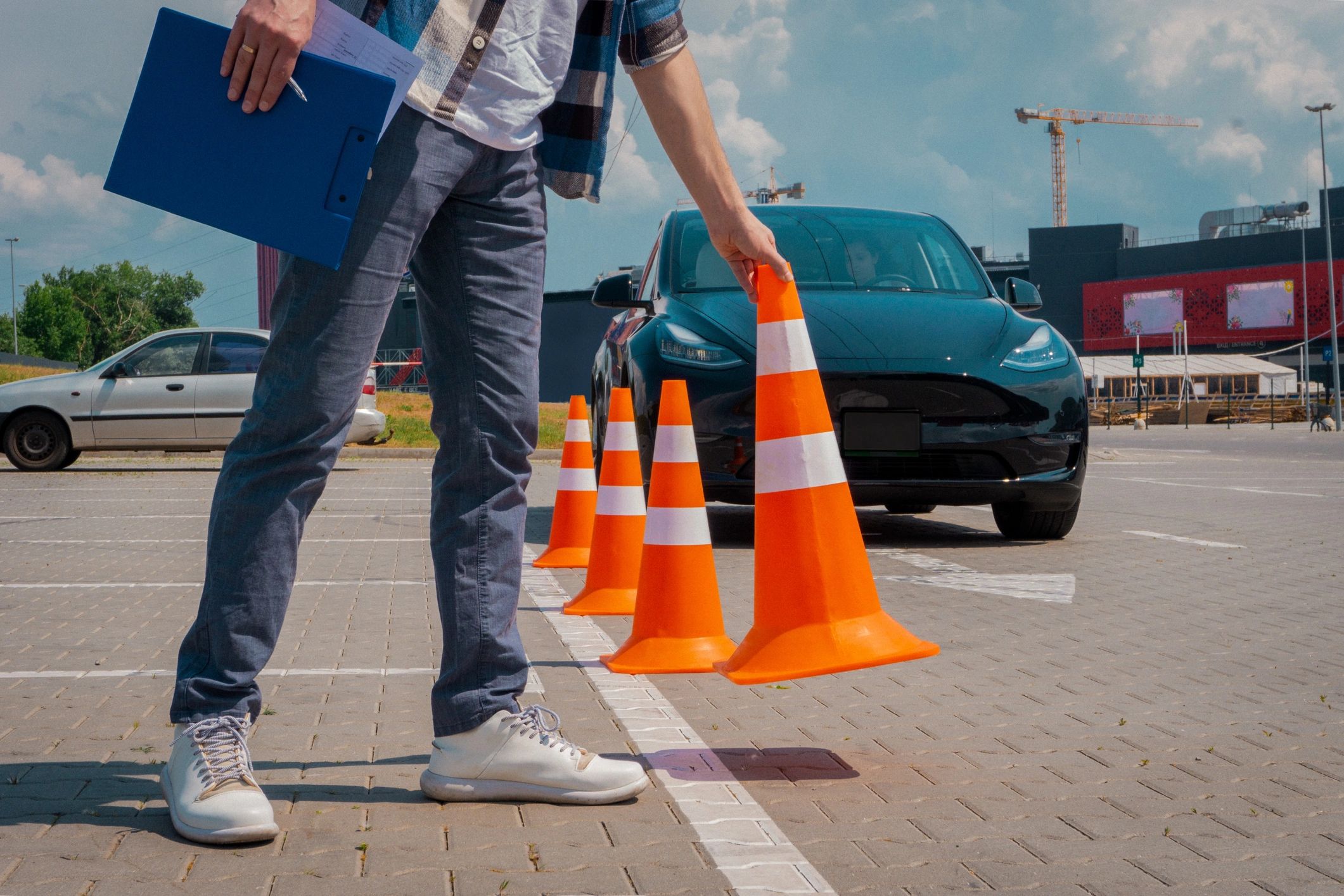 A person sets up traffic cones in a parking lot near a black car.