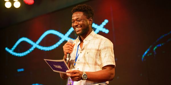 Man smiling while holding a microphone and note cards on stage.