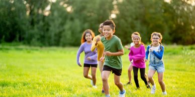 Five children running and playing outdoors on grass.