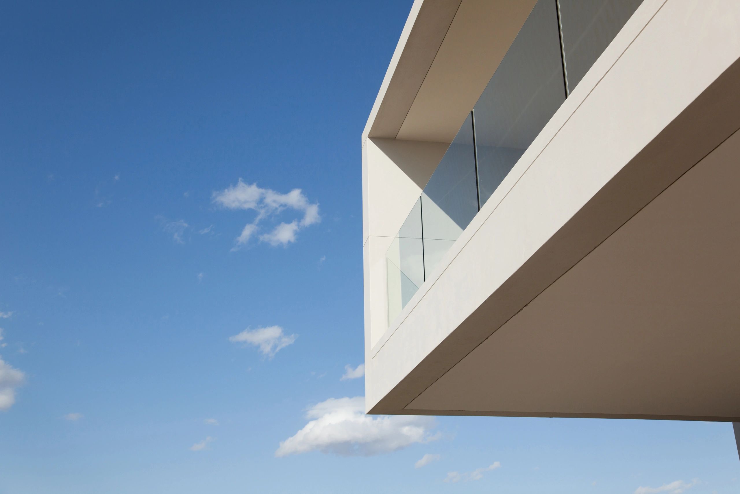 Minimalist modern building corner with glass balcony against blue sky.