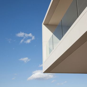 Detalle minimalista de edificio blanco con vidrio bajo un cielo azul.