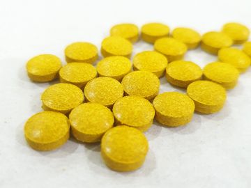 Close-up of round yellow tablets on a white surface.