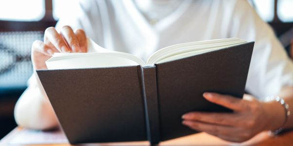 Person reading a book with a black cover.