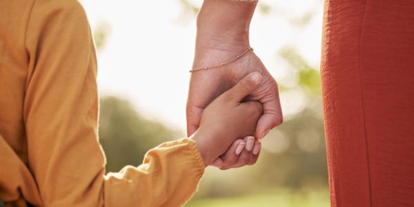 Adult and child holding hands outdoors.