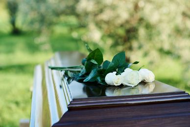 White roses lie on a closed wooden coffin outdoors.