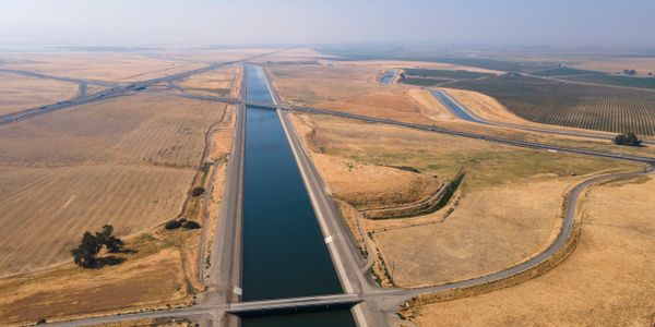 Aerial view of a canal running through dry farmland with a bridge crossing it.