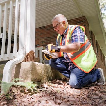 Inspector examines and documents wood damage on a house porch.