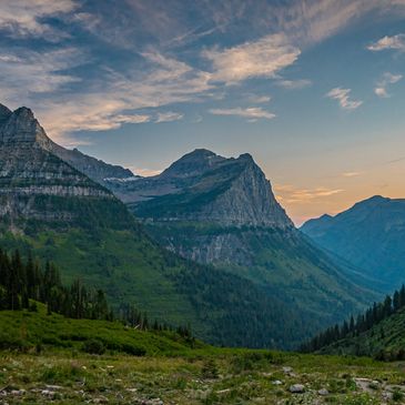 Sunset over a lush green valley surrounded by towering mountains.