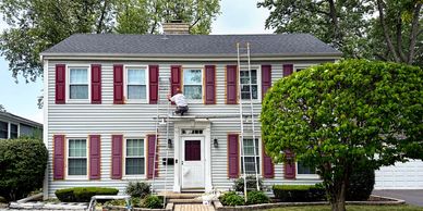 Man painting window shutters on a two-story house.