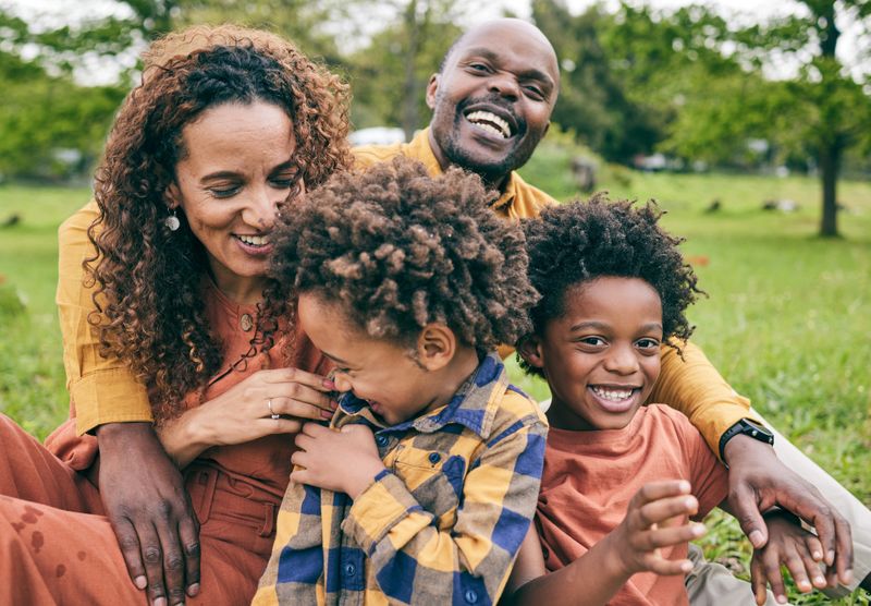 Happy family, parents and children in a park in summer, smile and relax on grass field for quality time, love and nature. Happiness, picnic and portrait of people outdoor and playing together