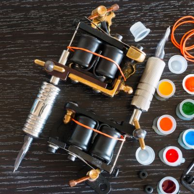 Two tattoo machines and colorful ink pots on a dark wooden surface.