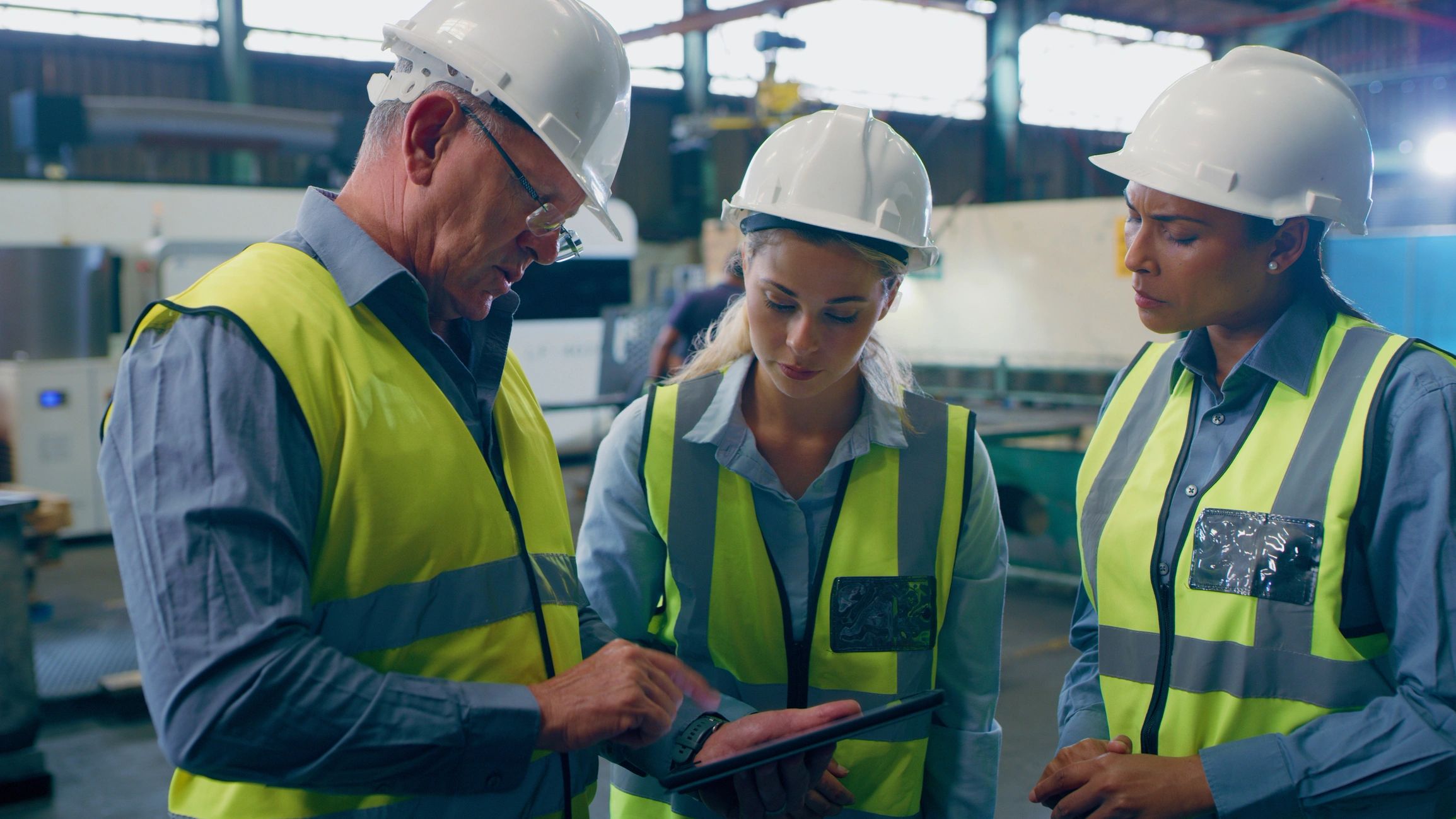 Three engineers in safety gear discussing plans in a factory.